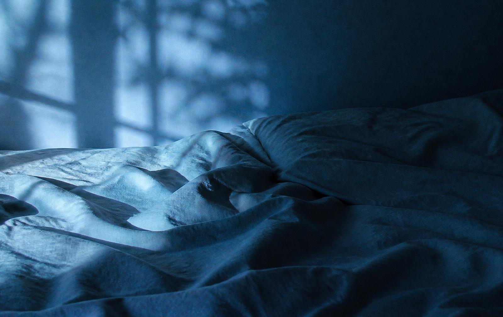 Rumpled bedsheets in cool pre-dawn light
